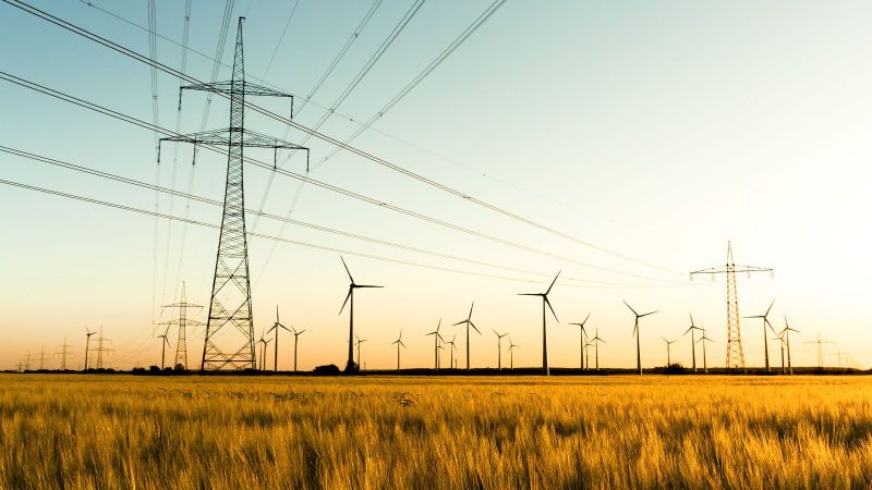 Das Bild zeigt Strommasten und Windräder vor einem weiten Horizont.