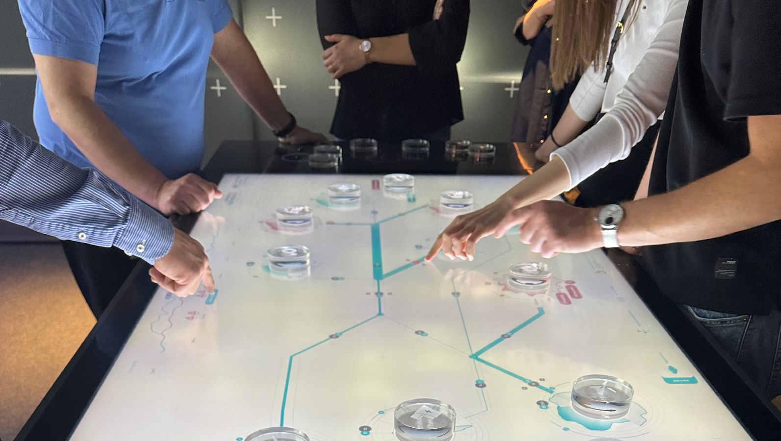 Das Bild zeigt die Hände und Arme mehrerer Personen, die auf einem interaktiven Tisch Glaselemente hin- und herschieben.