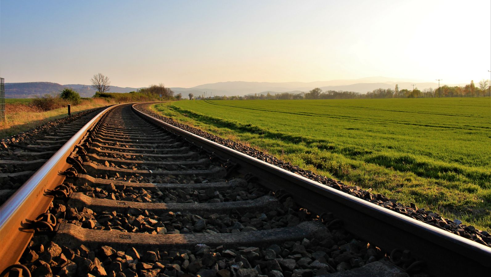 Das Bild zeigt in den Horizont laufende Bahnschienen im Dämmerlicht.