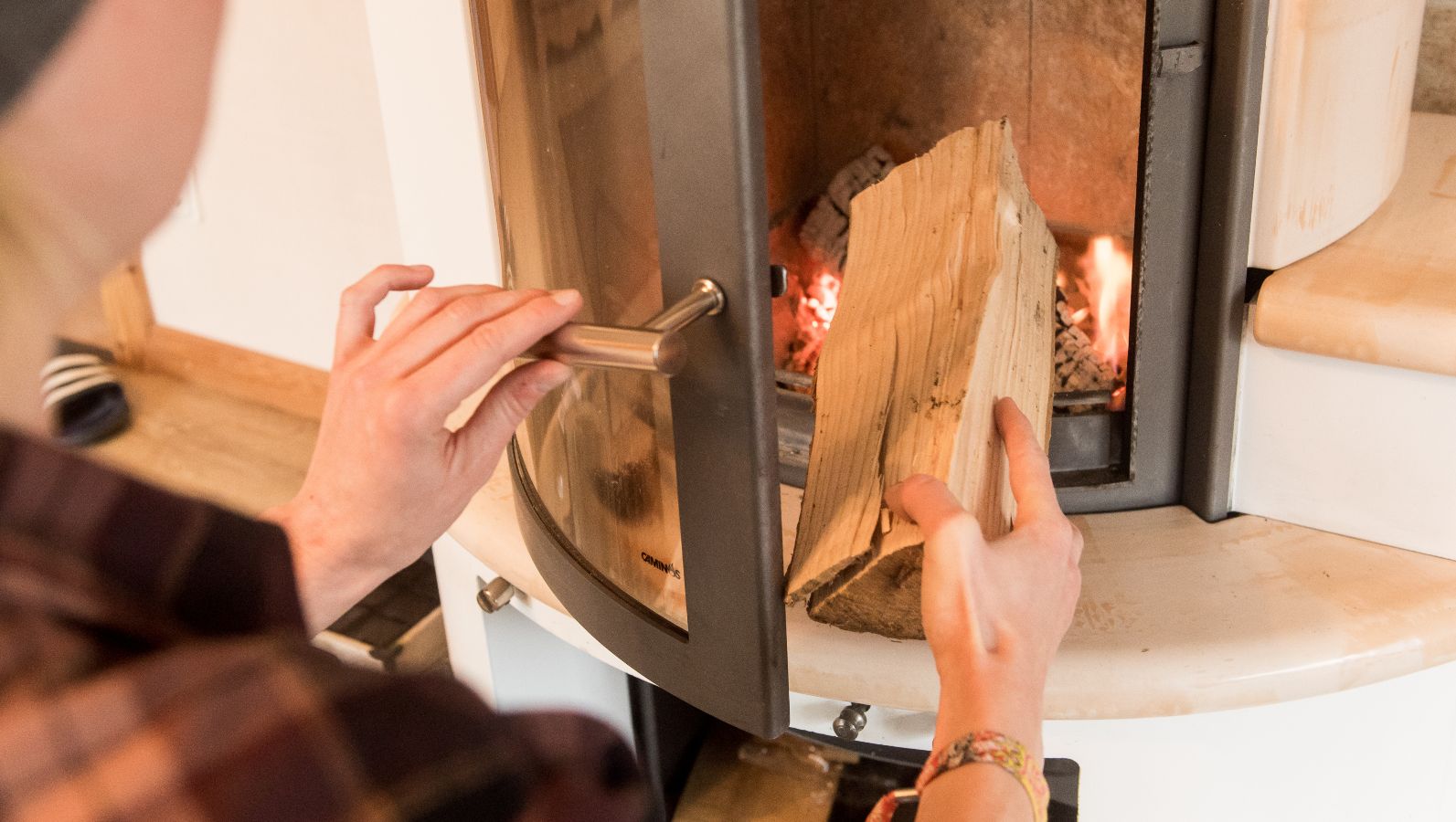 Das Bild zeigt einen Menschen, der einen Holzscheit in einen Kaminofen legt.